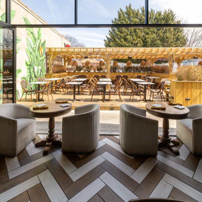 Indoor seating with two armchairs and a table, looking out to an outdoor patio with tables and chairs.