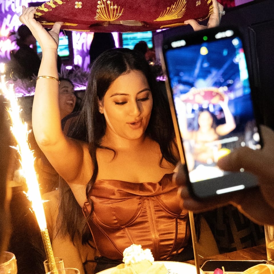A woman in a restaurant holds a sombrero overhead while another person photographs her.